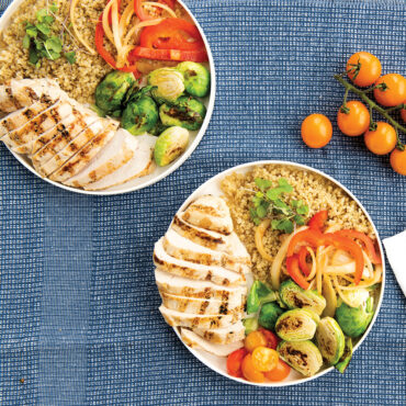 A overhead view of a white lunch plate on a blue placemat. The plate contains a serving of food. With cherry tomatoes to the side.